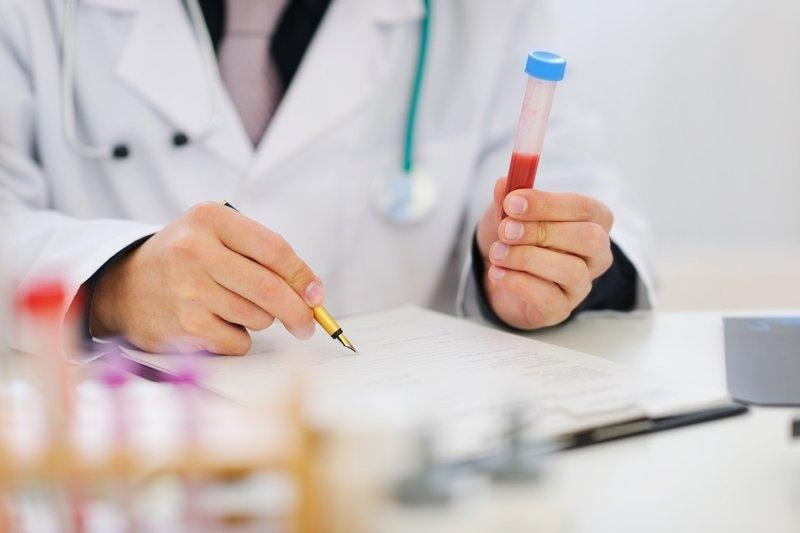 Healthcare professional holding blood sample tube and writing notes