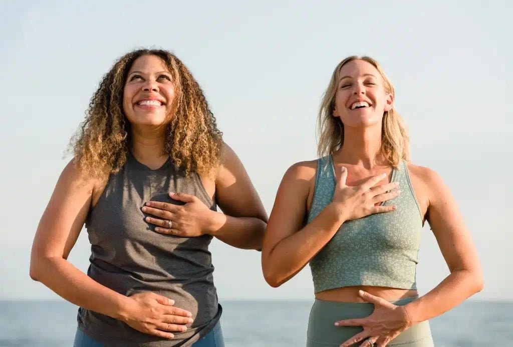 Two women smiling outdoors holding their stomach and heart