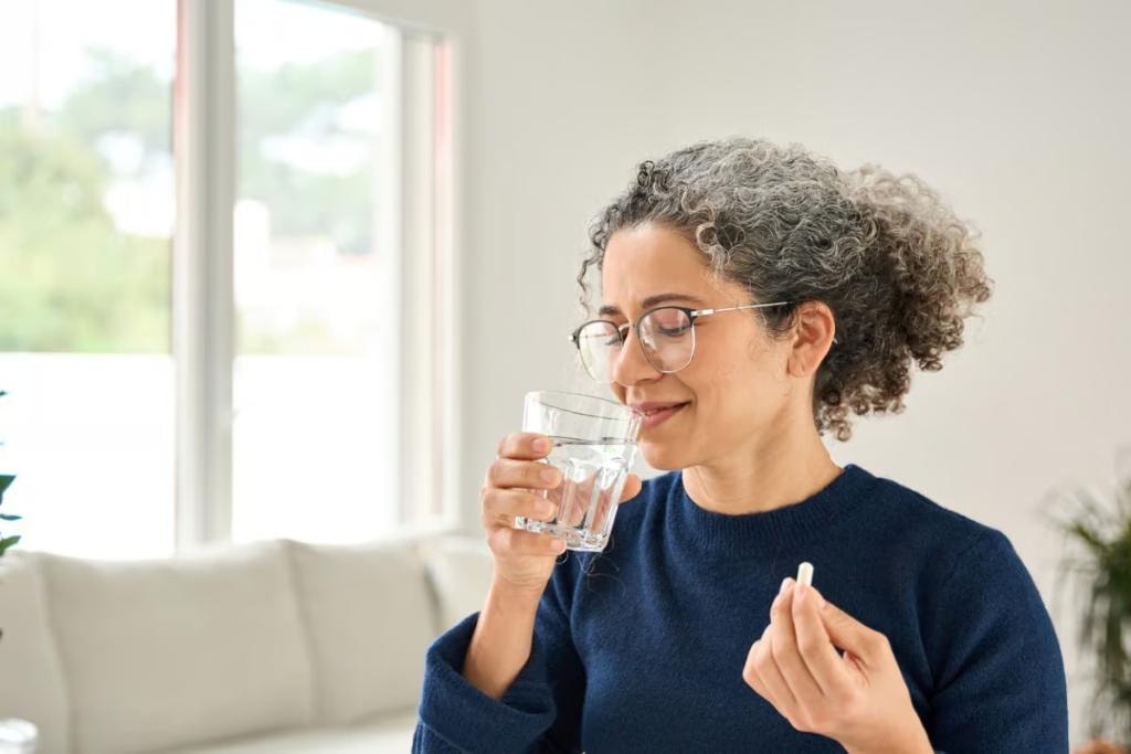 Woman drinking water and taking a pill indoors